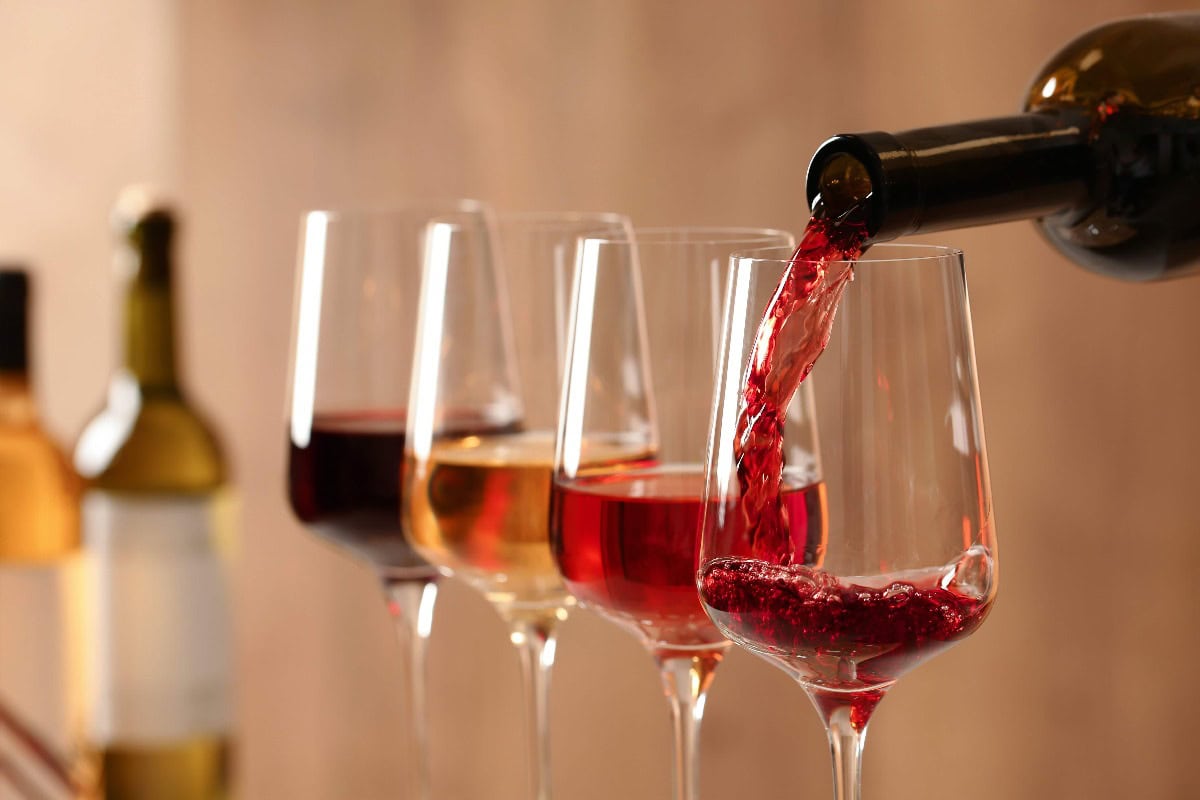 Einschenken von Wein aus der Flasche in ein Glas auf unscharfem Hintergrund, nah