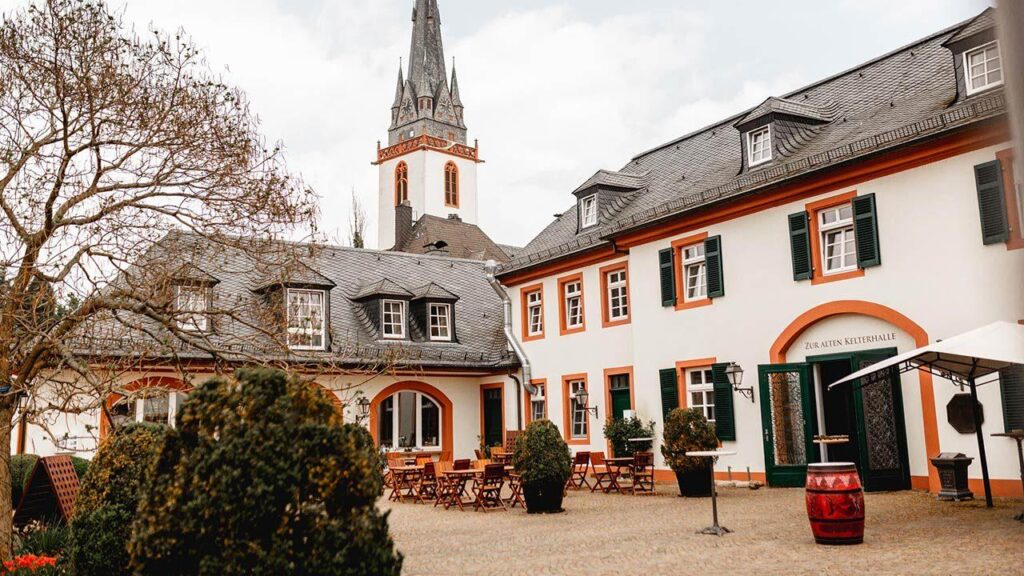 Ein malerischer, historischer Innenhof mit Tischen, umgeben von roten und weißen Gebäuden.